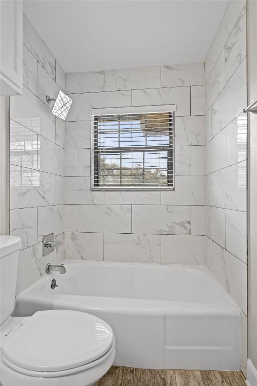 bathroom with tub / shower combination, toilet, and wood finished floors