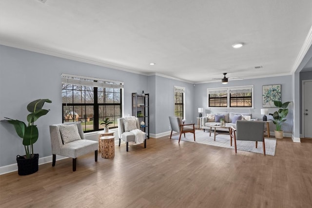 living area with crown molding, wood finished floors, baseboards, and ceiling fan