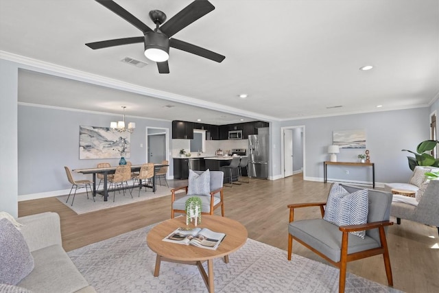 living room featuring a chandelier, light wood-style floors, a ceiling fan, baseboards, and crown molding