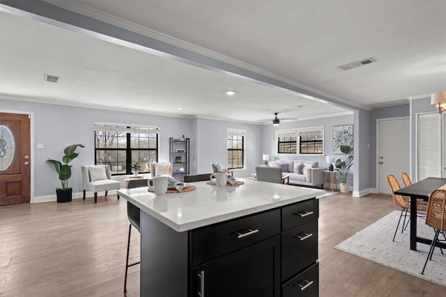kitchen with dark cabinetry, a breakfast bar, light countertops, ornamental molding, and light wood finished floors