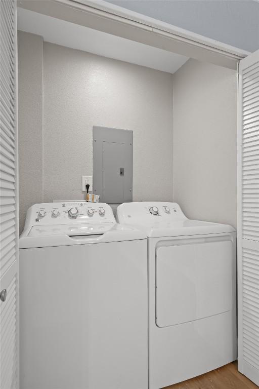 clothes washing area with electric panel, laundry area, wood finished floors, and separate washer and dryer