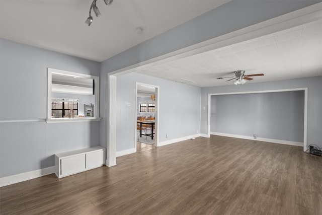 unfurnished living room featuring baseboards, dark wood-type flooring, and a ceiling fan