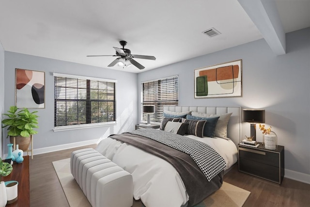 bedroom featuring a ceiling fan, wood finished floors, baseboards, visible vents, and beam ceiling