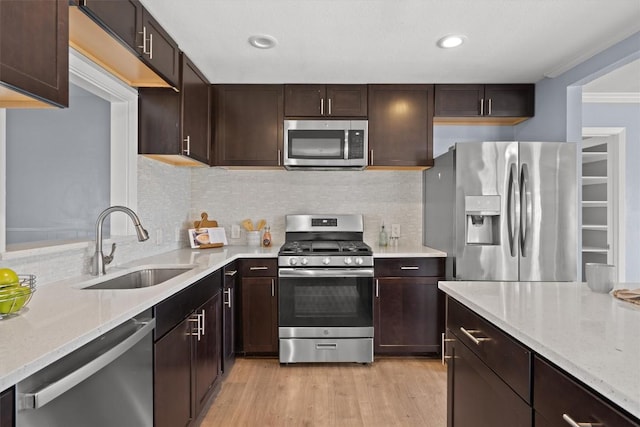 kitchen featuring stainless steel appliances, a sink, dark brown cabinetry, light wood-style floors, and crown molding