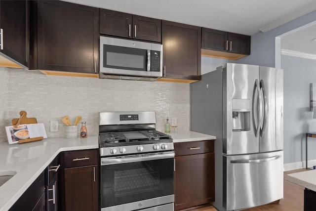 kitchen featuring ornamental molding, decorative backsplash, stainless steel appliances, dark brown cabinets, and light wood-style floors