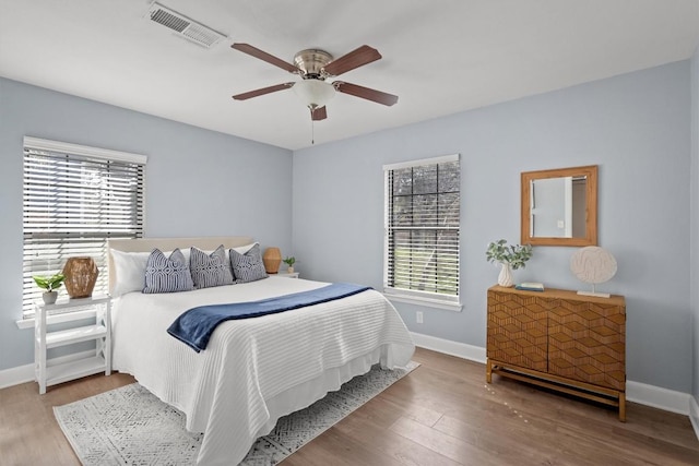 bedroom featuring visible vents, multiple windows, baseboards, and wood finished floors