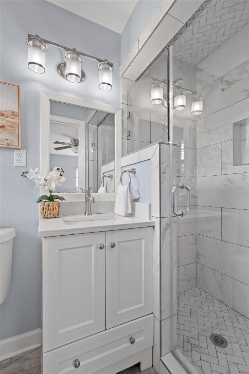 full bath with vanity, baseboards, ceiling fan, a shower stall, and toilet