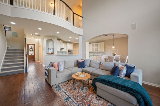 living area with visible vents, baseboards, stairway, a towering ceiling, and dark wood-style floors