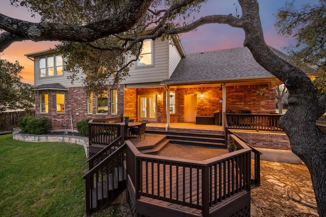 back of house featuring a lawn, fence, french doors, a shingled roof, and brick siding