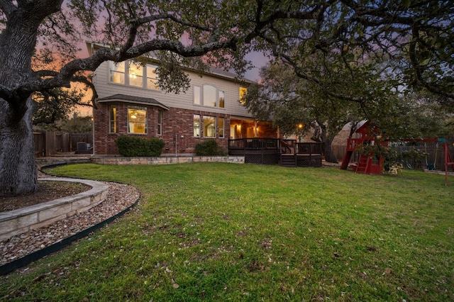 back of property featuring a fenced backyard, a deck, a playground, a lawn, and brick siding