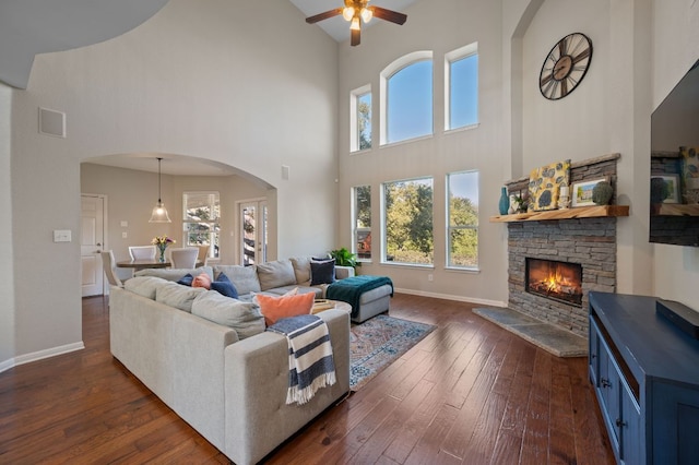 living room with a ceiling fan, dark wood finished floors, arched walkways, a fireplace, and baseboards