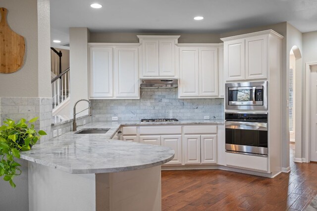 kitchen with dark wood finished floors, appliances with stainless steel finishes, a peninsula, arched walkways, and a sink