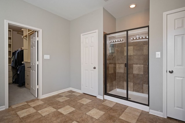 bathroom with a walk in closet, baseboards, and a stall shower