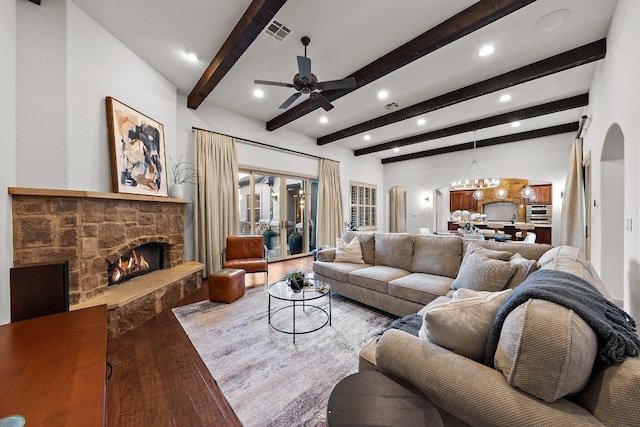 living room with wood finished floors, arched walkways, ceiling fan with notable chandelier, a stone fireplace, and visible vents