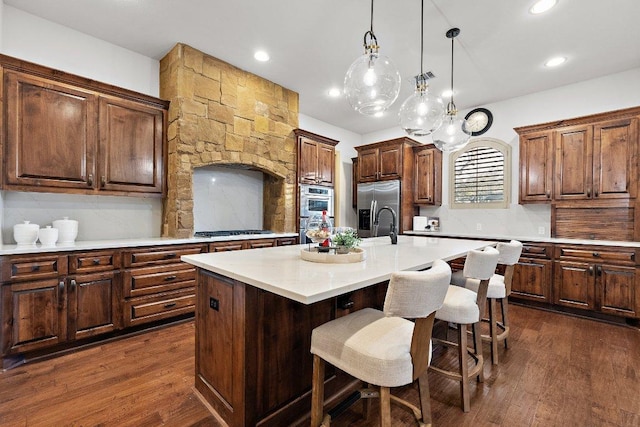 12500 Verandah Ct, Austin, TX 78726 - kitchen with stainless steel appliances, dark wood-type flooring, a center island with sink, light countertops, and a kitchen breakfast bar