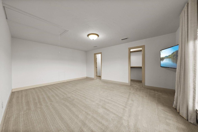 unfurnished bedroom featuring attic access, visible vents, a walk in closet, light carpet, and baseboards