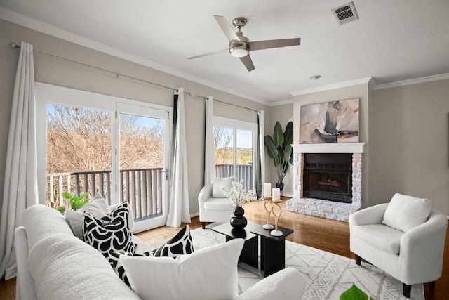 living area with visible vents, a fireplace with raised hearth, a ceiling fan, ornamental molding, and wood finished floors