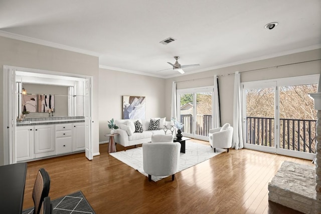 living area featuring visible vents, wood finished floors, crown molding, baseboards, and ceiling fan