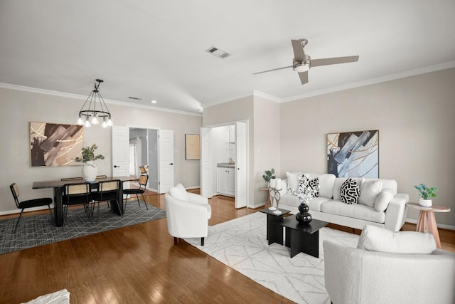 living area with ornamental molding, wood finished floors, visible vents, and baseboards