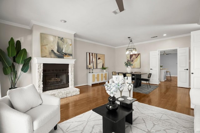 living area with wood finished floors, visible vents, baseboards, ornamental molding, and a stone fireplace