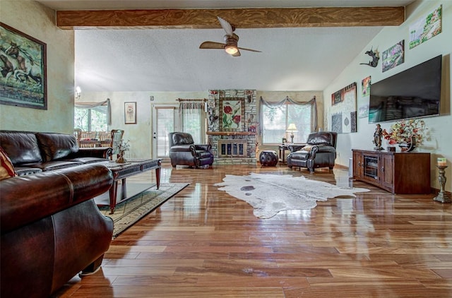 living area with a stone fireplace, lofted ceiling with beams, wood finished floors, and a textured ceiling