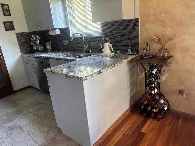 kitchen with a sink, baseboards, decorative backsplash, light stone countertops, and dishwasher