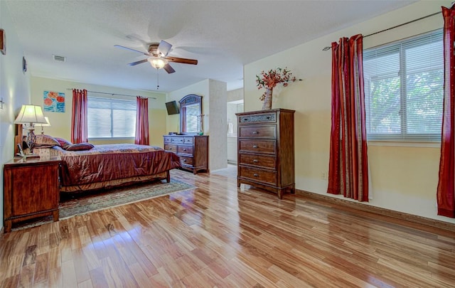 bedroom with light wood-type flooring, a textured ceiling, visible vents, and a ceiling fan