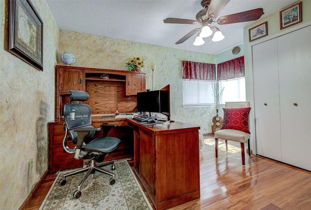 office area featuring wallpapered walls, a textured ceiling, ceiling fan, and wood finished floors