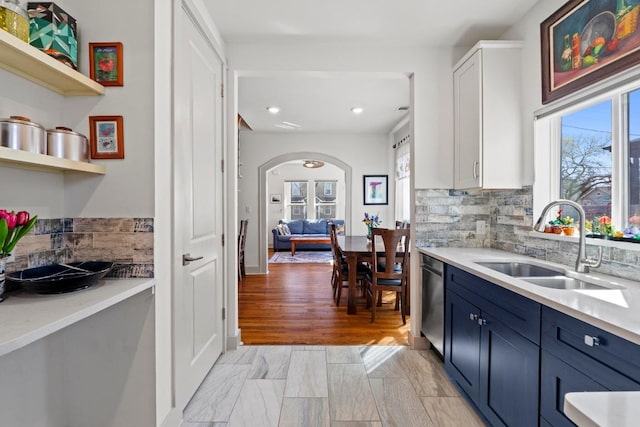 kitchen featuring a sink, backsplash, arched walkways, blue cabinets, and stainless steel dishwasher