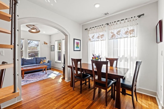 dining area featuring wood finished floors, visible vents, arched walkways, and baseboards