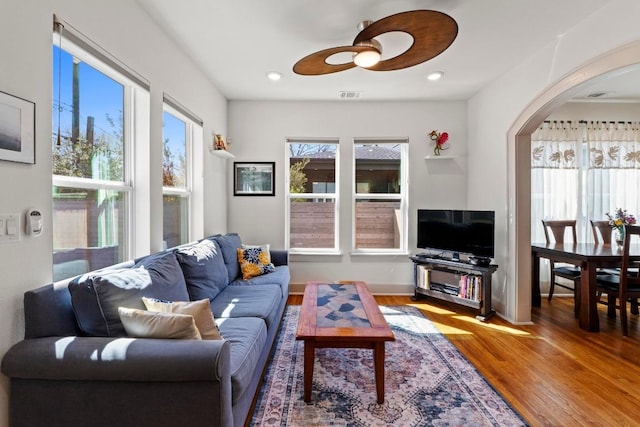 living area featuring visible vents, plenty of natural light, arched walkways, and wood finished floors