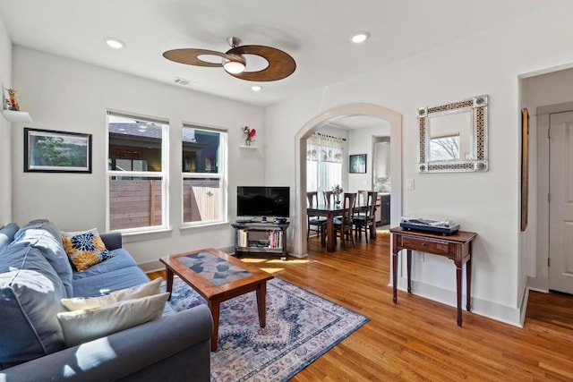 living room with visible vents, light wood finished floors, baseboards, recessed lighting, and arched walkways