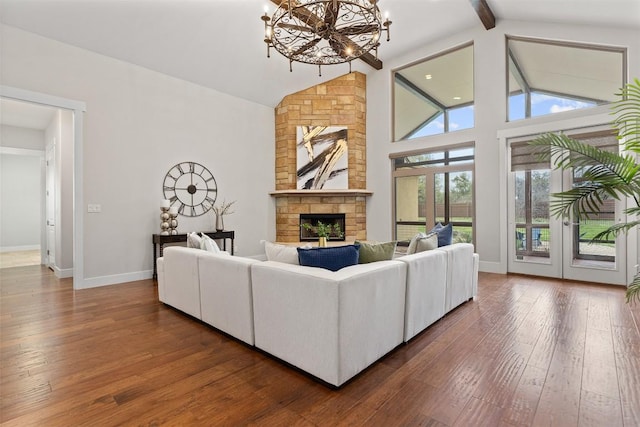 living room featuring a chandelier, a stone fireplace, dark wood-type flooring, beam ceiling, and baseboards