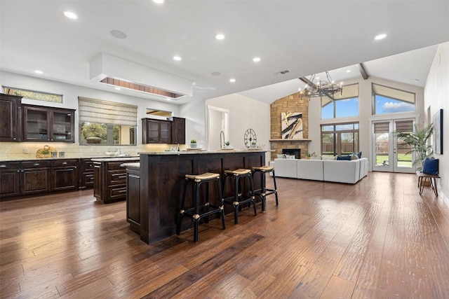 kitchen with a kitchen island with sink, a breakfast bar, a chandelier, dark brown cabinetry, and dark wood-style flooring