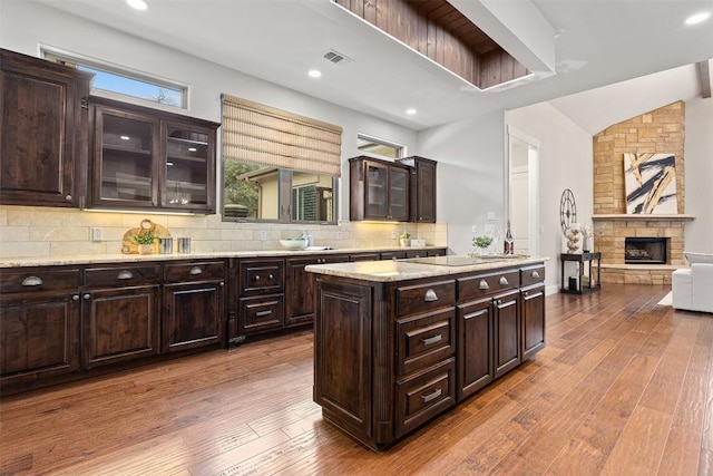 kitchen with a stone fireplace, dark brown cabinets, dark wood-style flooring, and backsplash