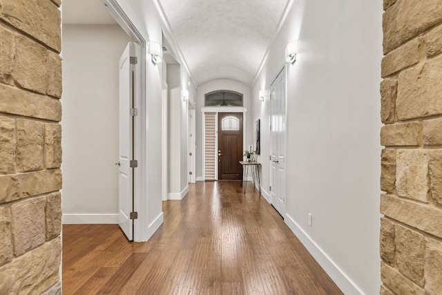 hallway featuring wood-type flooring, baseboards, and vaulted ceiling