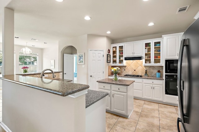 kitchen featuring visible vents, black appliances, an island with sink, tasteful backsplash, and extractor fan