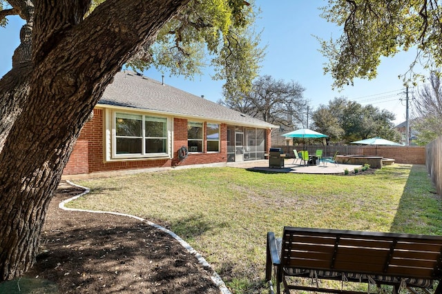 back of property with brick siding, a lawn, a fenced backyard, a sunroom, and a patio