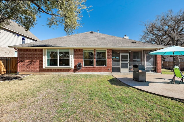 rear view of house featuring fence, a sunroom, a lawn, a patio area, and brick siding