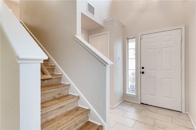 entrance foyer featuring tile patterned floors, visible vents, stairway, and baseboards