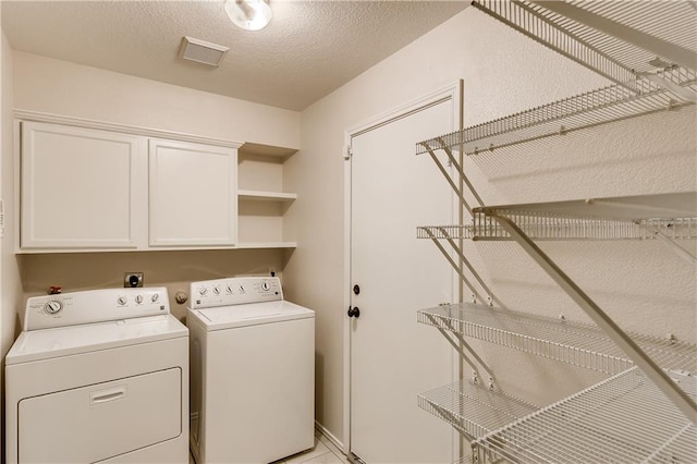 washroom with a textured ceiling, cabinet space, visible vents, and washer and clothes dryer