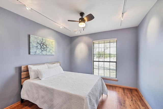 bedroom with rail lighting, baseboards, ceiling fan, and wood finished floors