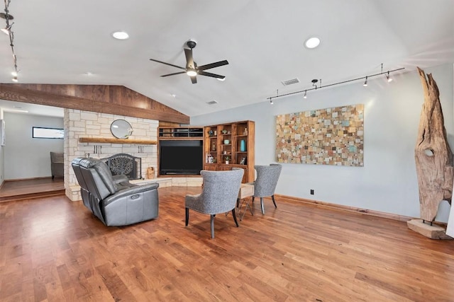 living area with track lighting, visible vents, lofted ceiling, a stone fireplace, and wood finished floors