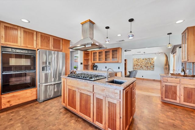 kitchen with an island with sink, island exhaust hood, light stone counters, a sink, and stainless steel appliances