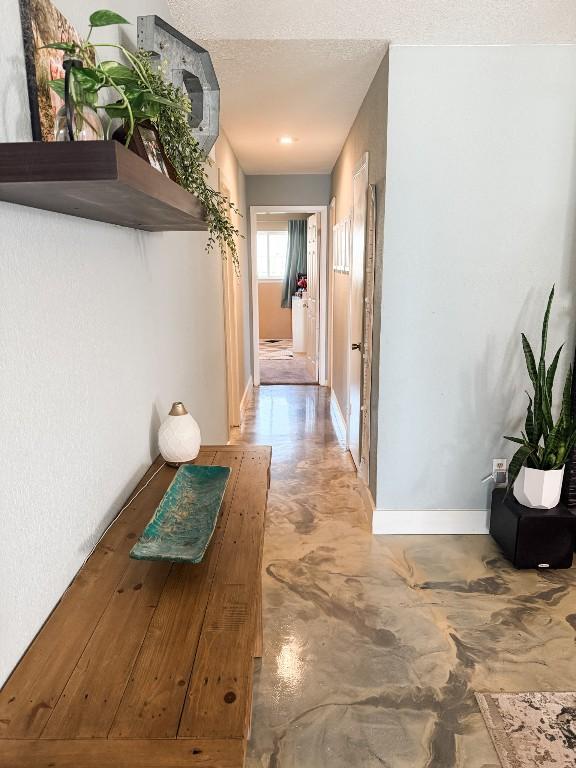 corridor with concrete floors, baseboards, and a textured ceiling