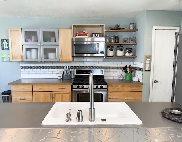 kitchen featuring glass insert cabinets, light brown cabinets, dark countertops, stainless steel appliances, and decorative backsplash