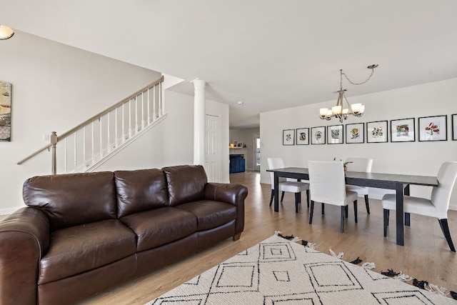 living room featuring stairway, an inviting chandelier, wood finished floors, and ornate columns