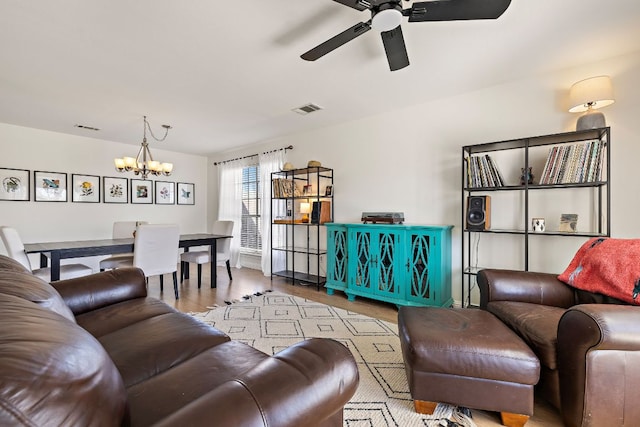 living room with ceiling fan with notable chandelier, wood finished floors, and visible vents