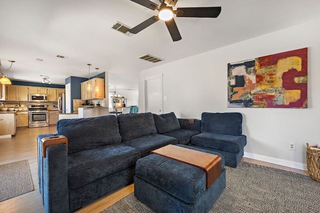 living area featuring visible vents, ceiling fan with notable chandelier, baseboards, and light wood finished floors