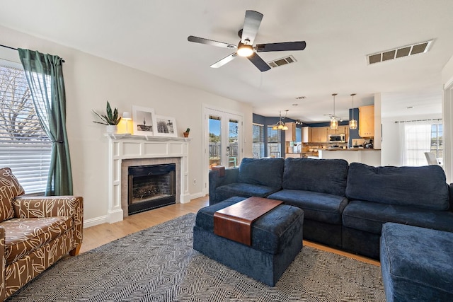 living room featuring visible vents, light wood-style flooring, a fireplace, and a ceiling fan